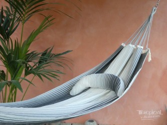 Coussin sur un hamac en tissu à rayures grises et blanches sur une terrasse tropicale