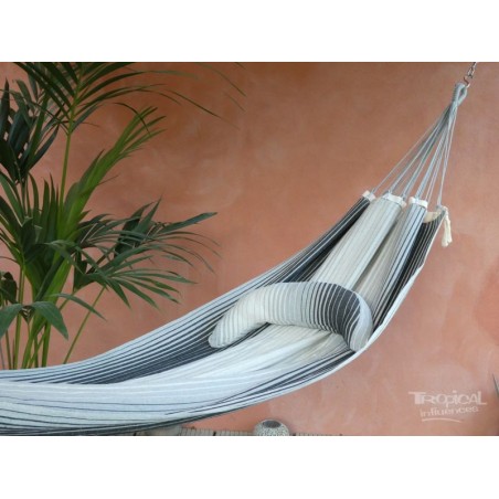 Coussin sur un hamac en tissu à rayures grises et blanches sur une terrasse tropicale