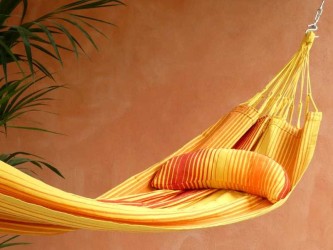 Coussin sur un hamac en tissu à rayures rouges et jaunes sur une terrasse tropicale