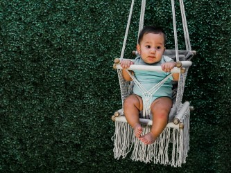 Bébé assis joyeusement dans hamac macramé écru en plein air