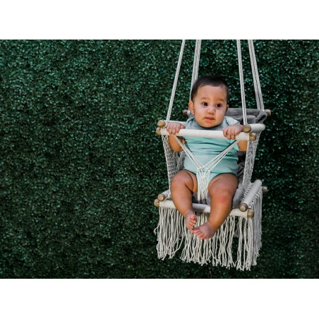 Bébé assis joyeusement dans hamac macramé écru en plein air