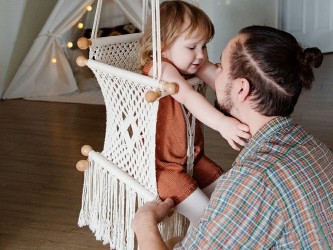 Tendre interaction entre un père et son bébé dans un hamac en macramé brut à l'intérieur d'une maison