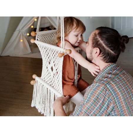 Tendre interaction entre un père et son bébé dans un hamac en macramé brut à l'intérieur d'une maison