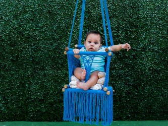 Bébé dans un transat avec un enfant assis, vue de face sur fond vert