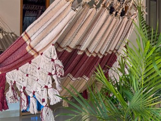 Hamac bordeaux suspendu entre palmiers, avec franges artisanales en coton