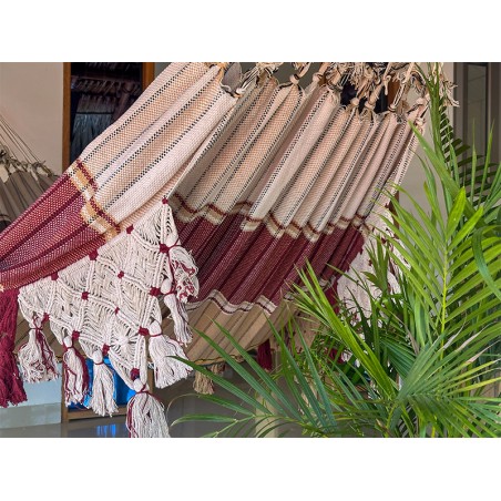 Hamac bordeaux suspendu entre palmiers, avec franges artisanales en coton