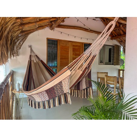 Hamac colombien XL suspendu sur un porche, montrant son design à rayures et motifs dans des tons chauds