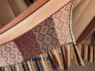 Gros plan du motif artisanal détaillé et des franges aux extrémités du hamac, dans une palette harmonieuse de couleurs terre