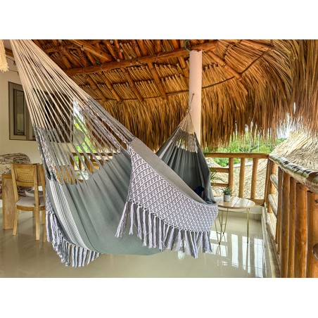 Hamac colombien taille L en coton dans les tons gris-vert doux et blanc suspendu sur un porche, montrant les franges décoratives
