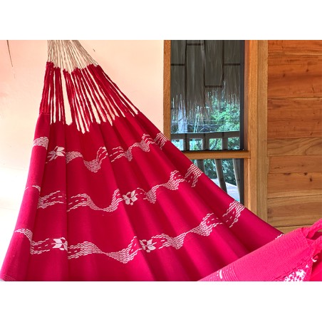 Grand hamac colombien XL dans des tons rouges intenses, suspendu sur un porche, montrant son design audacieux