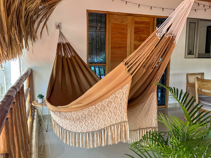Hamac de luxe XXL DUNA dans un jardin tropical, couleur naturelle avec franges, parfait pour la détente en extérieur Hamac de luxe XXL DUNA dans un jardin tropical, couleur naturelle avec franges, parfait pour la détente en extérieur