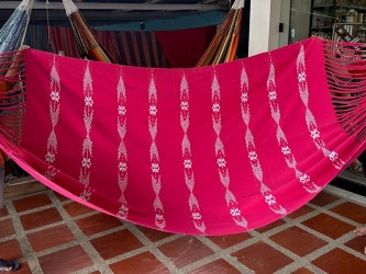 Hamac colombien XL avec son tissu rouge vibrant et le motif brodé distinctif des bords, exposant son design unique et artistique