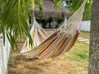 Le hamac L Elisa installé en extérieur, idéal pour les siestes à l’ombre, avec son design rayé coloré et apaisant