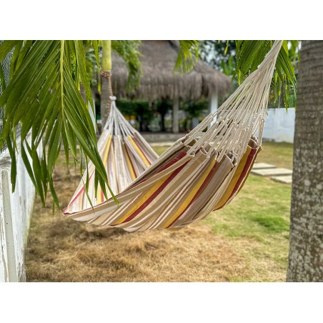 Le hamac L Elisa installé en extérieur, idéal pour les siestes à l’ombre, avec son design rayé coloré et apaisant