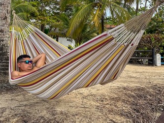 Homme se reposant dans un hamac L en Colombie, aux rayures jaunes, bordeaux et sable. Un modèle sobre et naturel
