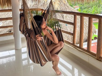 Femme profitant du confort d’une chaise hamac XXL, installée sous un toit en chaume. Confort éthique et durable