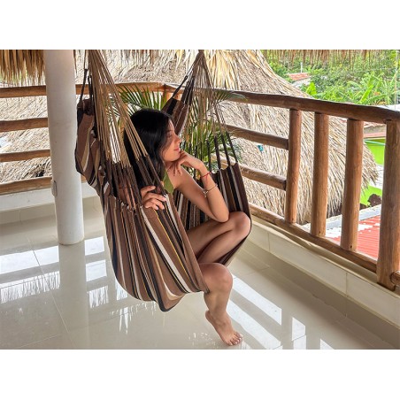 Femme profitant du confort d’une chaise hamac XXL, installée sous un toit en chaume. Confort éthique et durable