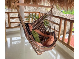 Femme détendue dans une hamac chaise XXL suspendue sur une terrasse en bois, ambiance tropicale
