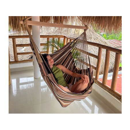 Femme détendue dans une hamac chaise XXL suspendue sur une terrasse en bois, ambiance tropicale