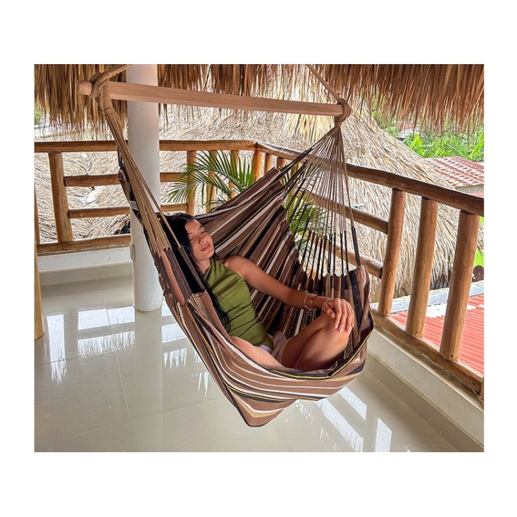 Femme détendue dans une hamac chaise XXL suspendue sur une terrasse en bois, ambiance tropicale