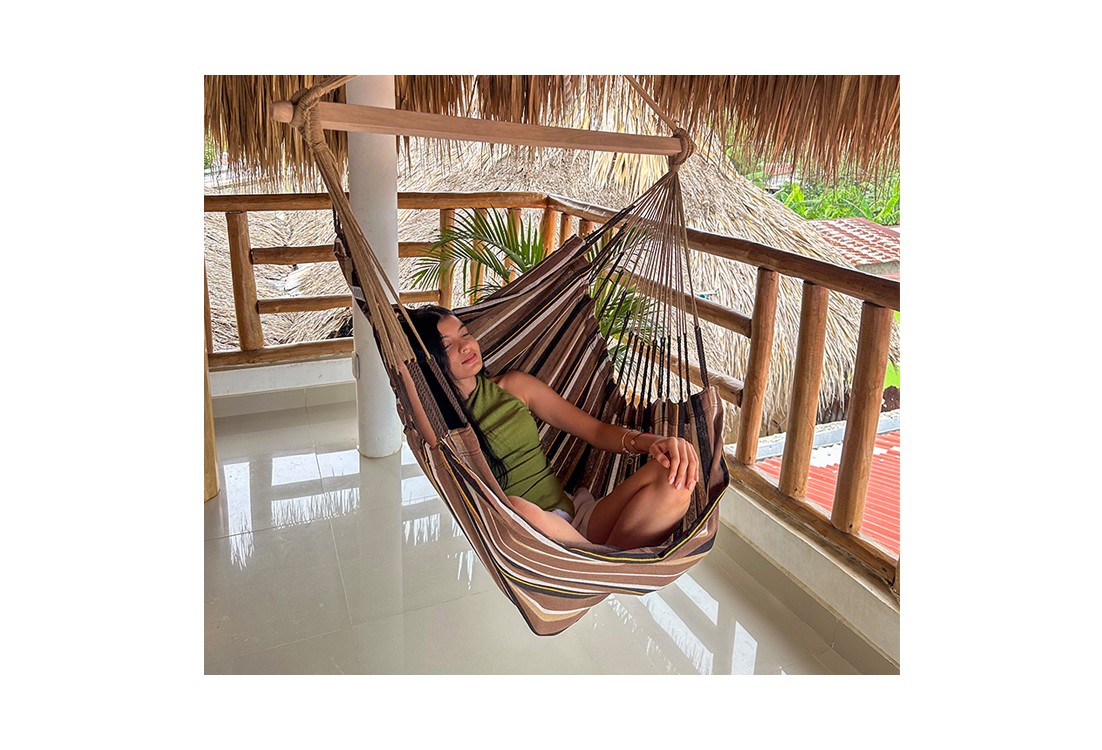 Femme détendue dans une hamac chaise XXL suspendue sur une terrasse en bois, ambiance tropicale