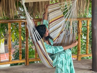 Femme installée dans un hamac chaise XXL en coton recyclé, rayures ocre et beige