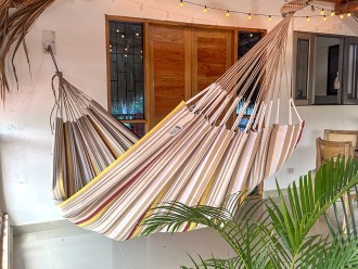 Hamac XXL installé sur une terrasse tropicale, idéal pour les siestes à l’ombre, avec son design rayé coloré et apaisant