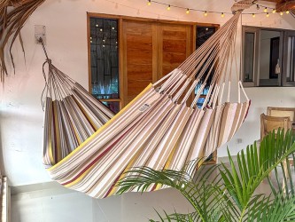 Hamac XXL installé sur une terrasse tropicale, idéal pour les siestes à l’ombre, avec son design rayé coloré et apaisant
