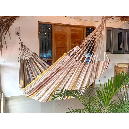 Hamac XXL installé sur une terrasse tropicale, idéal pour les siestes à l’ombre, avec son design rayé coloré et apaisant