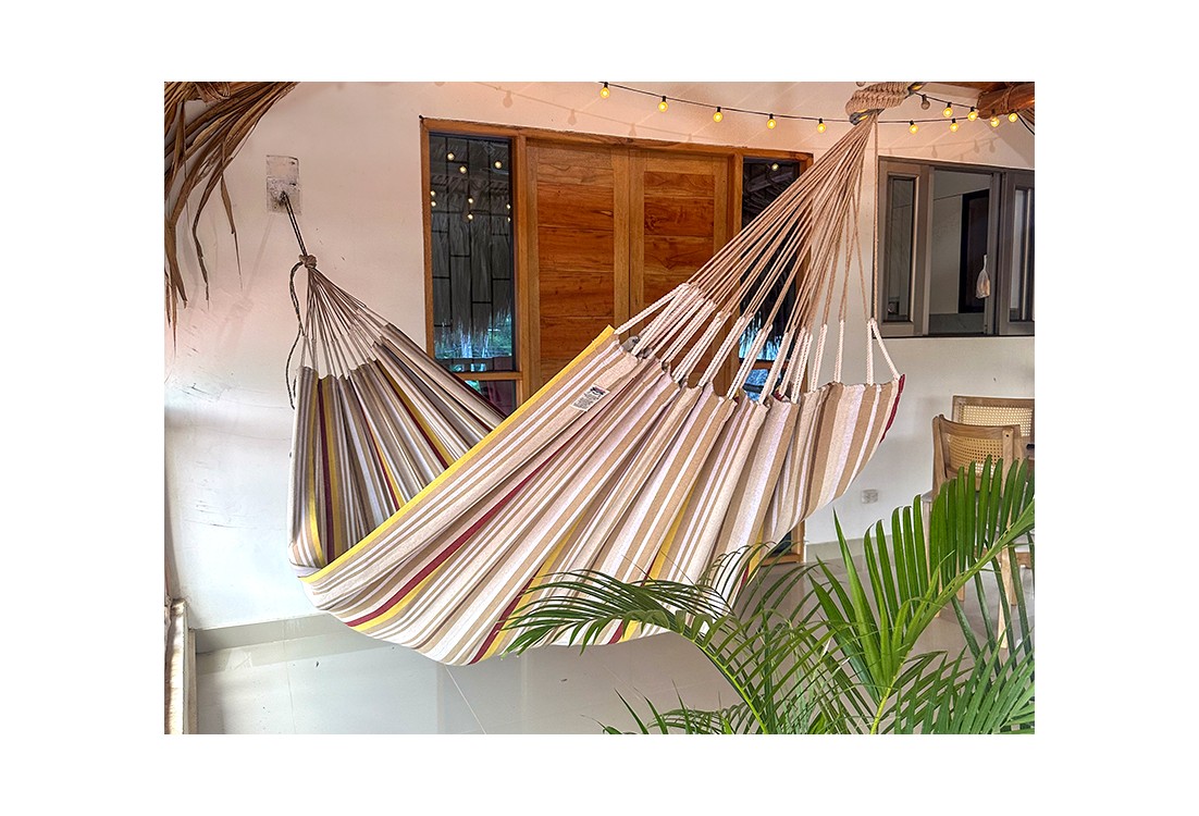 Hamac XXL installé sur une terrasse tropicale, idéal pour les siestes à l’ombre, avec son design rayé coloré et apaisant