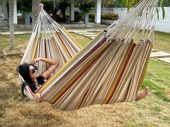 Moment de détente dans une hamac L, aux rayures jaunes, bordeaux et sable. Un modèle colombien à l’élégance naturelle
