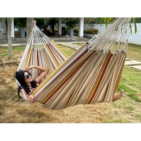 Moment de détente dans une hamac L, aux rayures jaunes, bordeaux et sable. Un modèle colombien à l’élégance naturelle