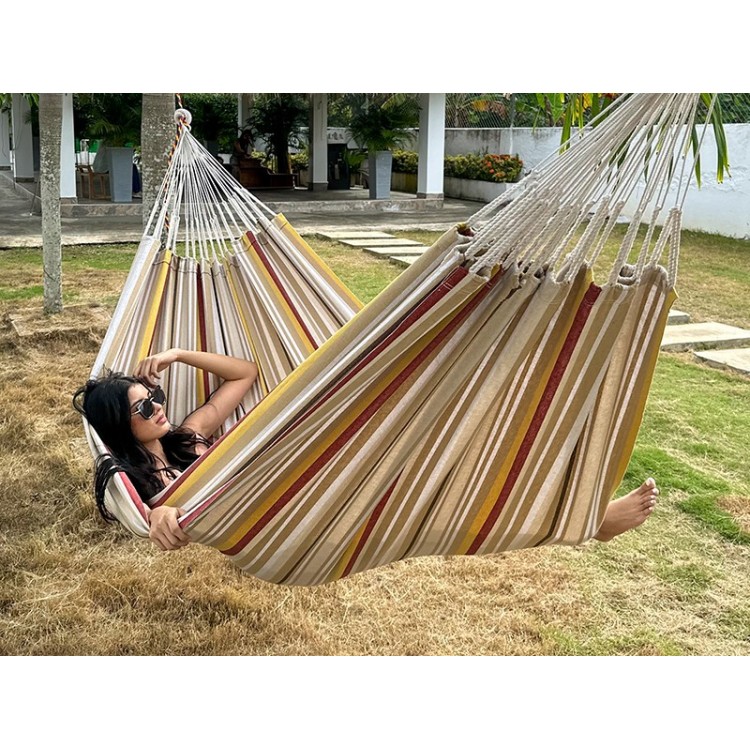Moment de détente dans une hamac L, aux rayures jaunes, bordeaux et sable. Un modèle colombien à l’élégance naturelle