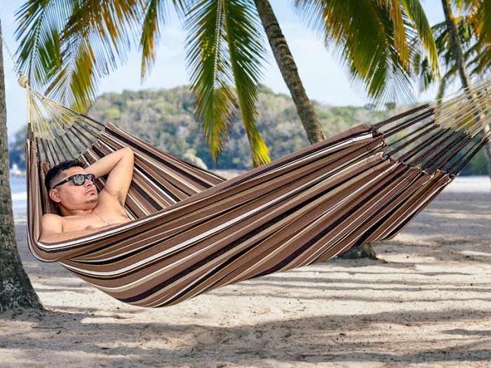 Homme se reposant dans hamac écologique suspendu entre deux cocotiers, sur fond de plage en Colombie