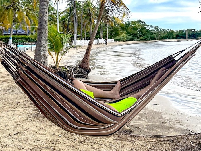 Homme se reposant dans hamac écologique suspendu entre deux cocotiers, sur fond de plage en Colombie