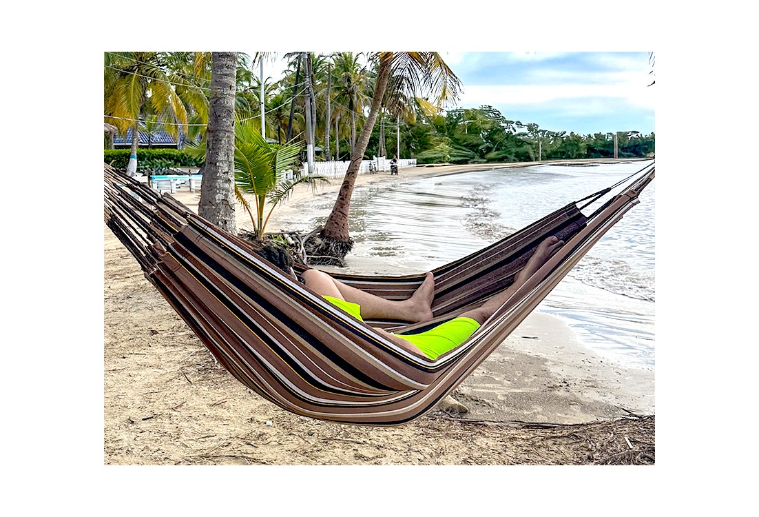 Homme se reposant dans hamac écologique suspendu entre deux cocotiers, sur fond de plage en Colombie