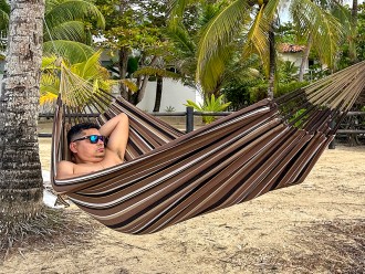 Homme se reposant dans hamac écologique suspendu entre deux cocotiers, sur fond de plage en Colombie