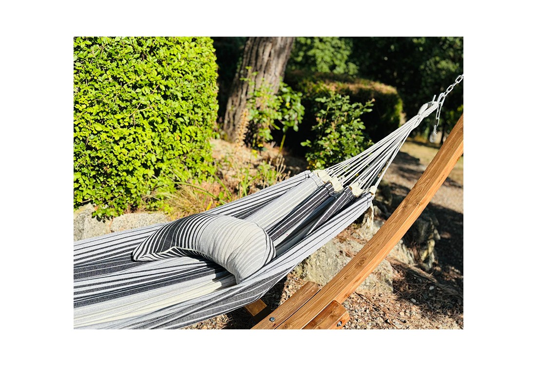 Coussin sur un hamac en tissu à rayures grises et blanches est suspendu dans un jardin