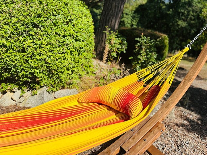 Coussin sur un hamac en tissu à rayures rouges et jaunes est suspendu dans un jardin