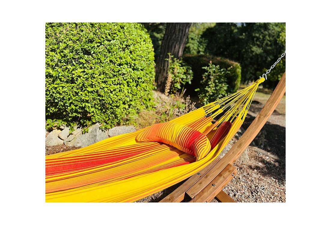 Coussin sur un hamac en tissu à rayures rouges et jaunes est suspendu dans un jardin