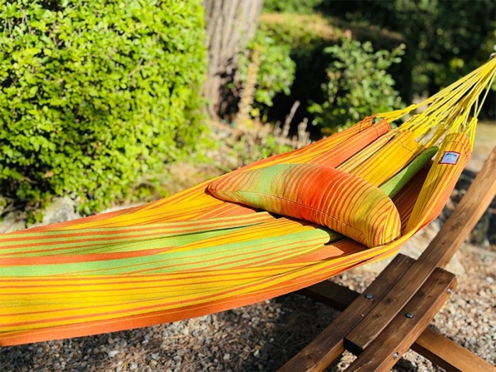 Coussin sur un hamac en tissu à rayures verts et oranges est suspendu dans un jardin