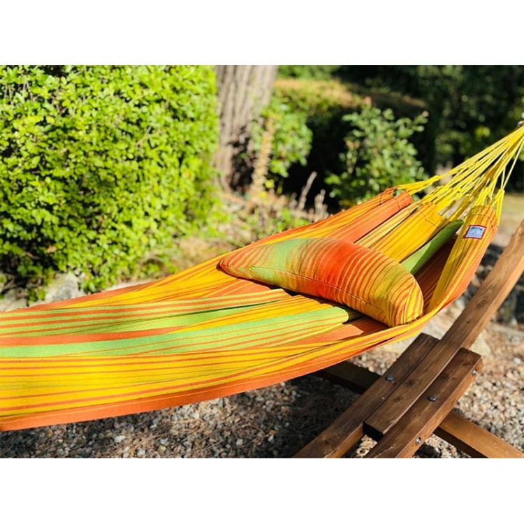 Coussin sur un hamac en tissu à rayures verts et oranges est suspendu dans un jardin