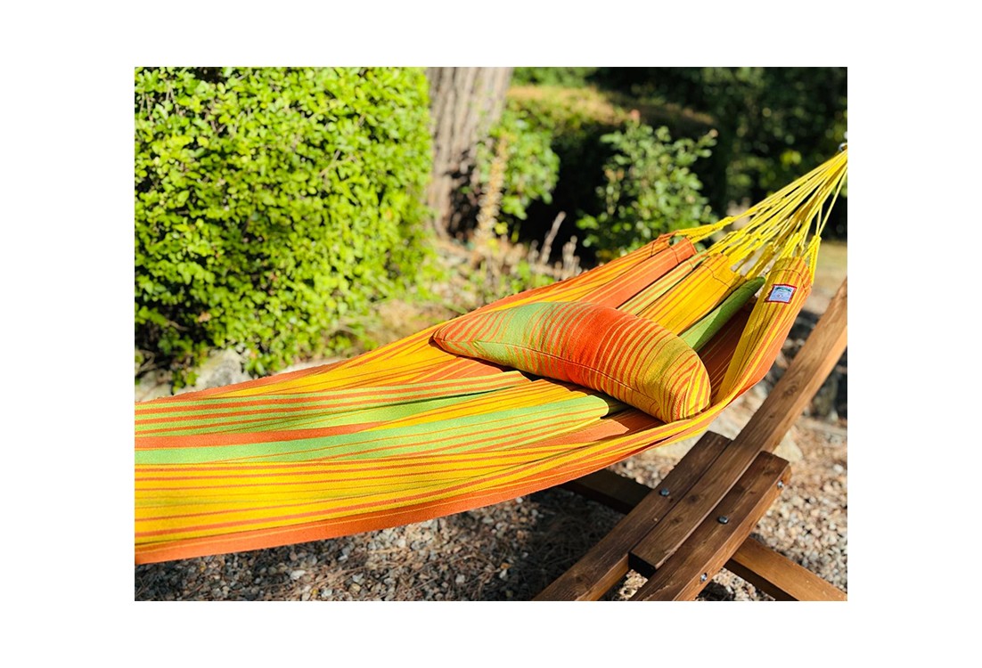 Coussin sur un hamac en tissu à rayures verts et oranges est suspendu dans un jardin