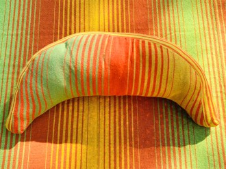 Coussin sur un hamac en tissu à rayures verts et oranges, sur un tissu de texture similaire