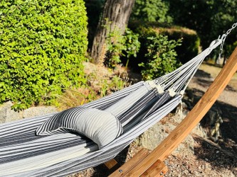 Coussin sur un hamac en tissu à rayures grises et blanches est suspendu dans un jardin