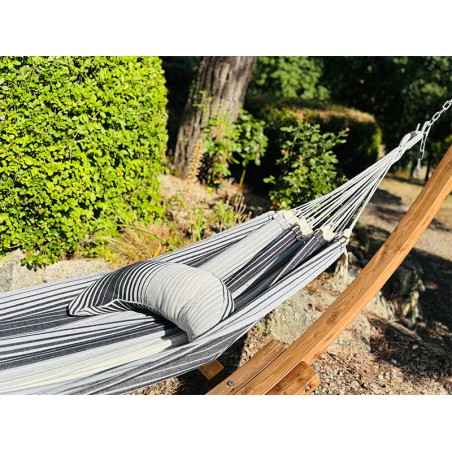 Coussin sur un hamac en tissu à rayures grises et blanches est suspendu dans un jardin