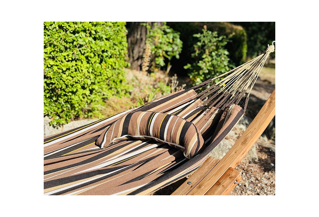 Coussin sur un hamac en tissu à rayures marron et blanches est suspendu dans un jardin