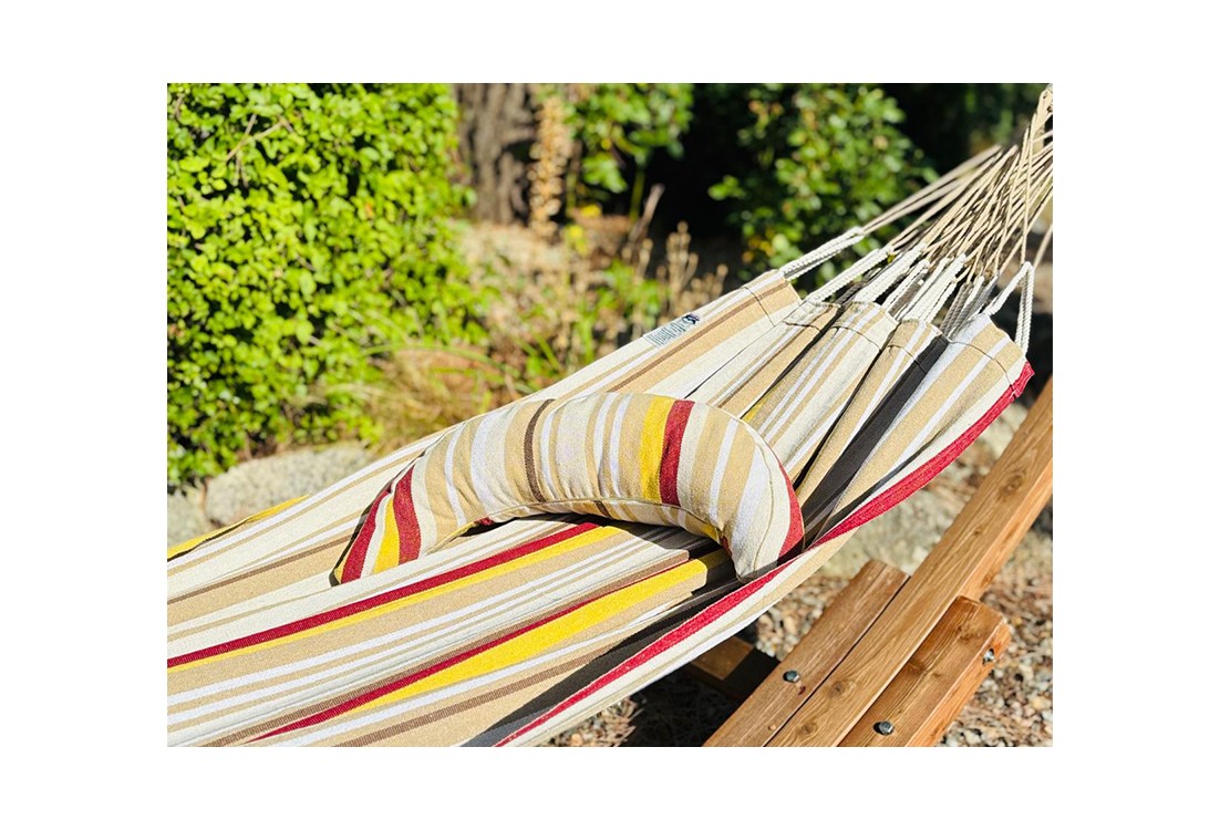 Coussin sur un hamac en tissu à rayures beiges, grenat, ocre et blanc est suspendu dans un jardin