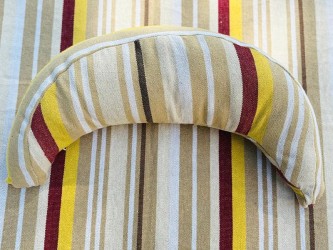 Coussin sur un hamac en tissu à rayures beige, grenat, ocre et blanc, sur un tissu de texture similaire