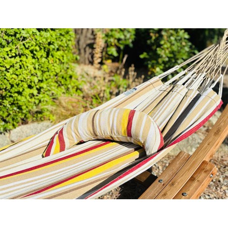Coussin sur un hamac en tissu à rayures beiges, grenat, ocre et blanc est suspendu dans un jardin